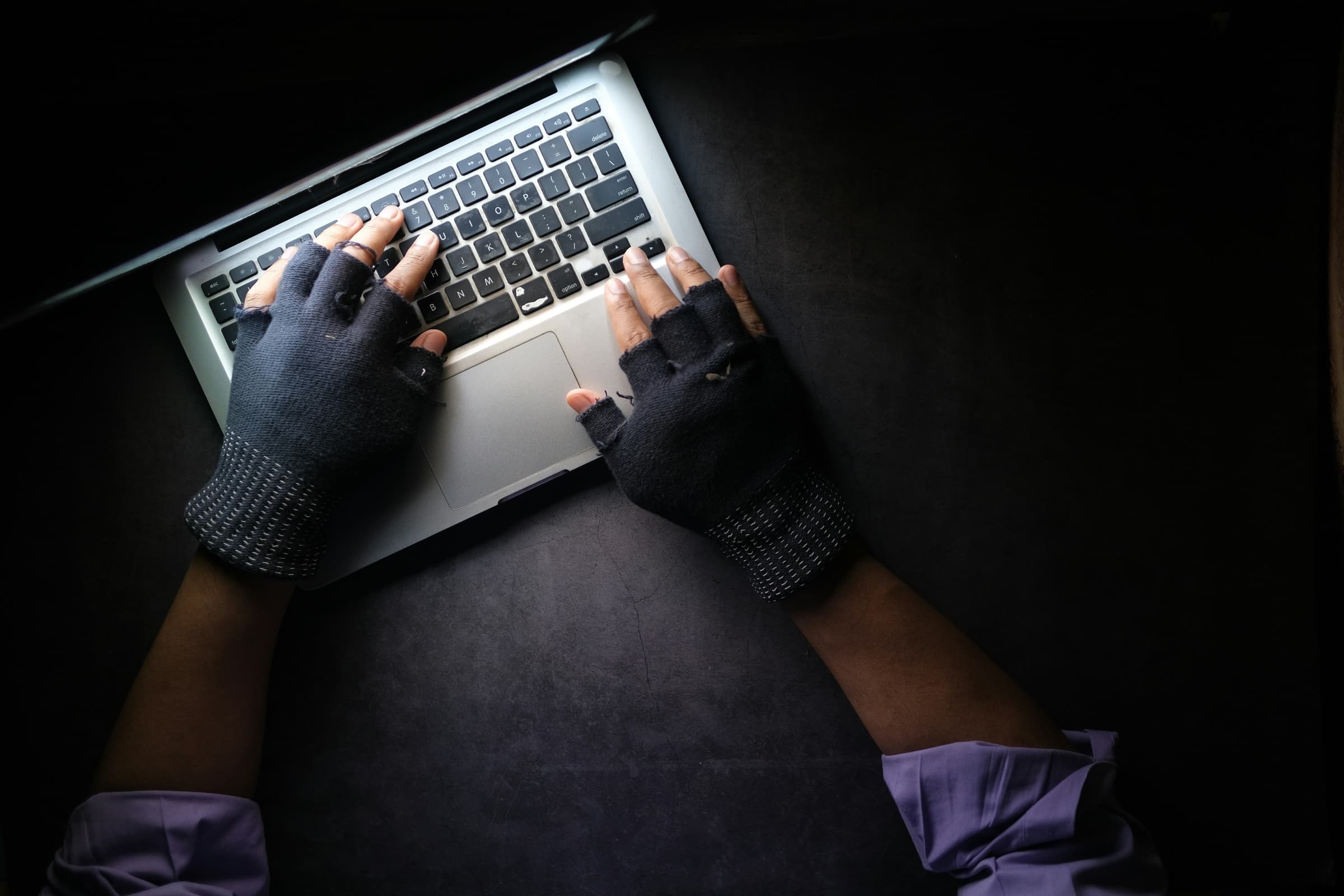 Hands in fingerless gloves typing on a laptop in the dark