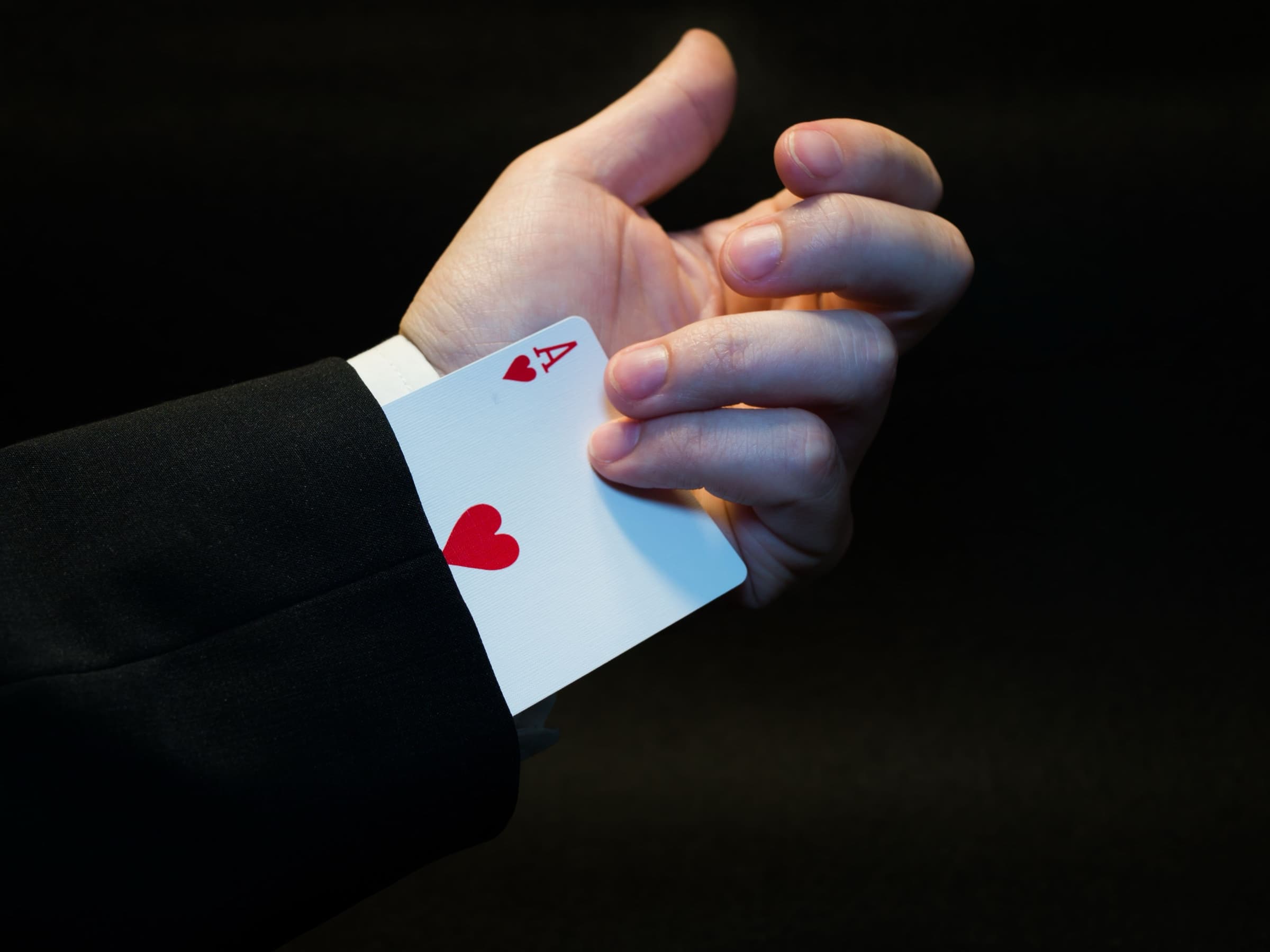 A hand pulling an ace of hearts out of a suit sleeve
