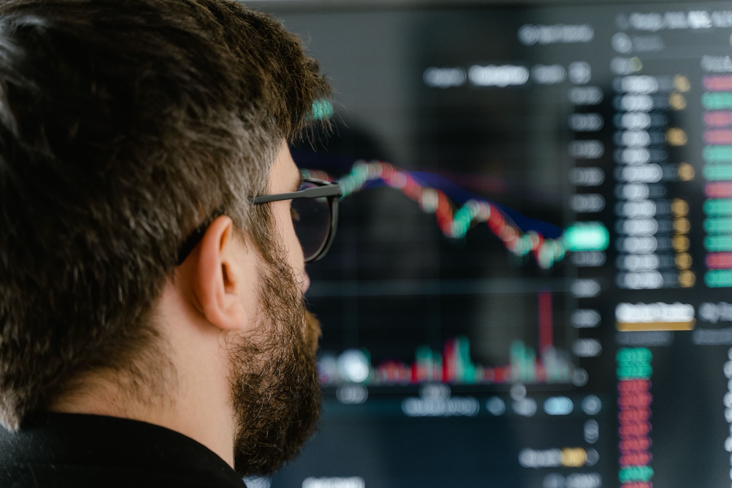 A man in glasses looking at charts and numbers on a large screen