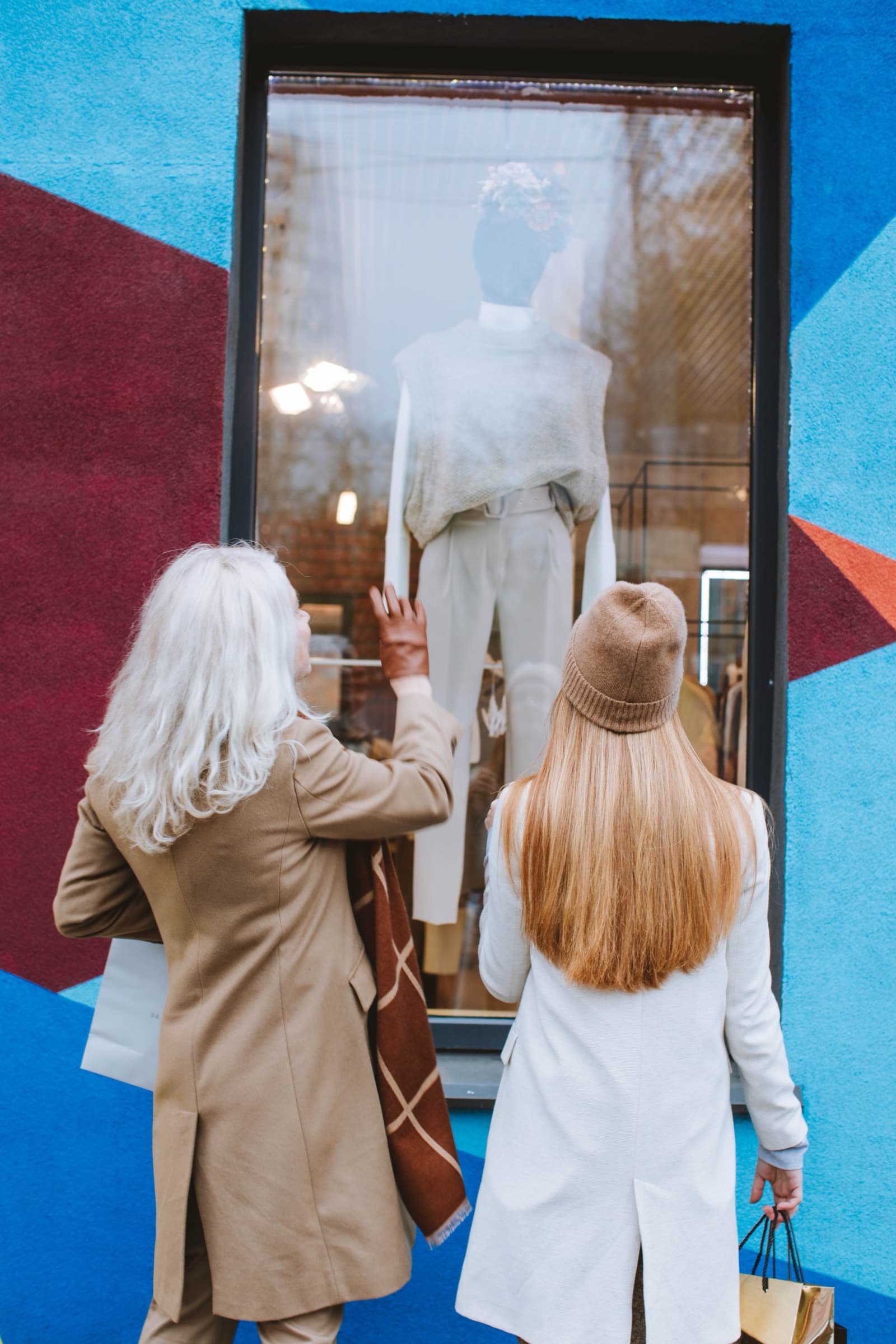 Two women with shopping bags looking at an outfit in a shop window
