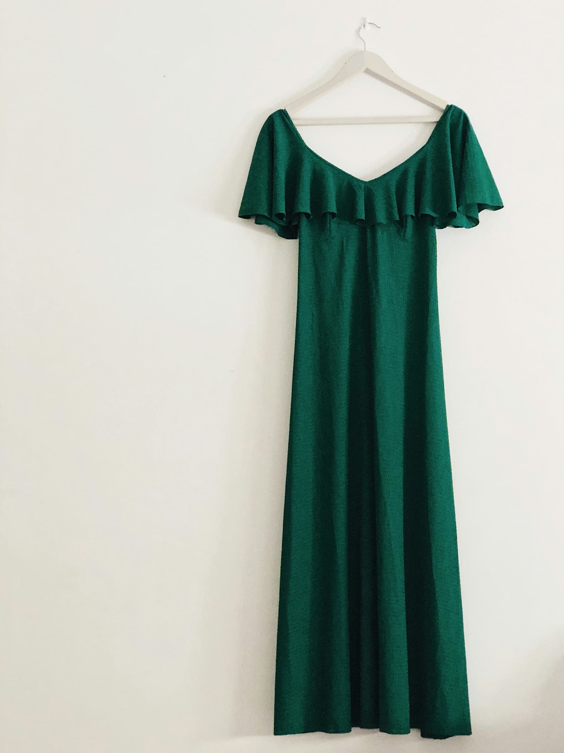 A long green dress hanging alone on a white wall