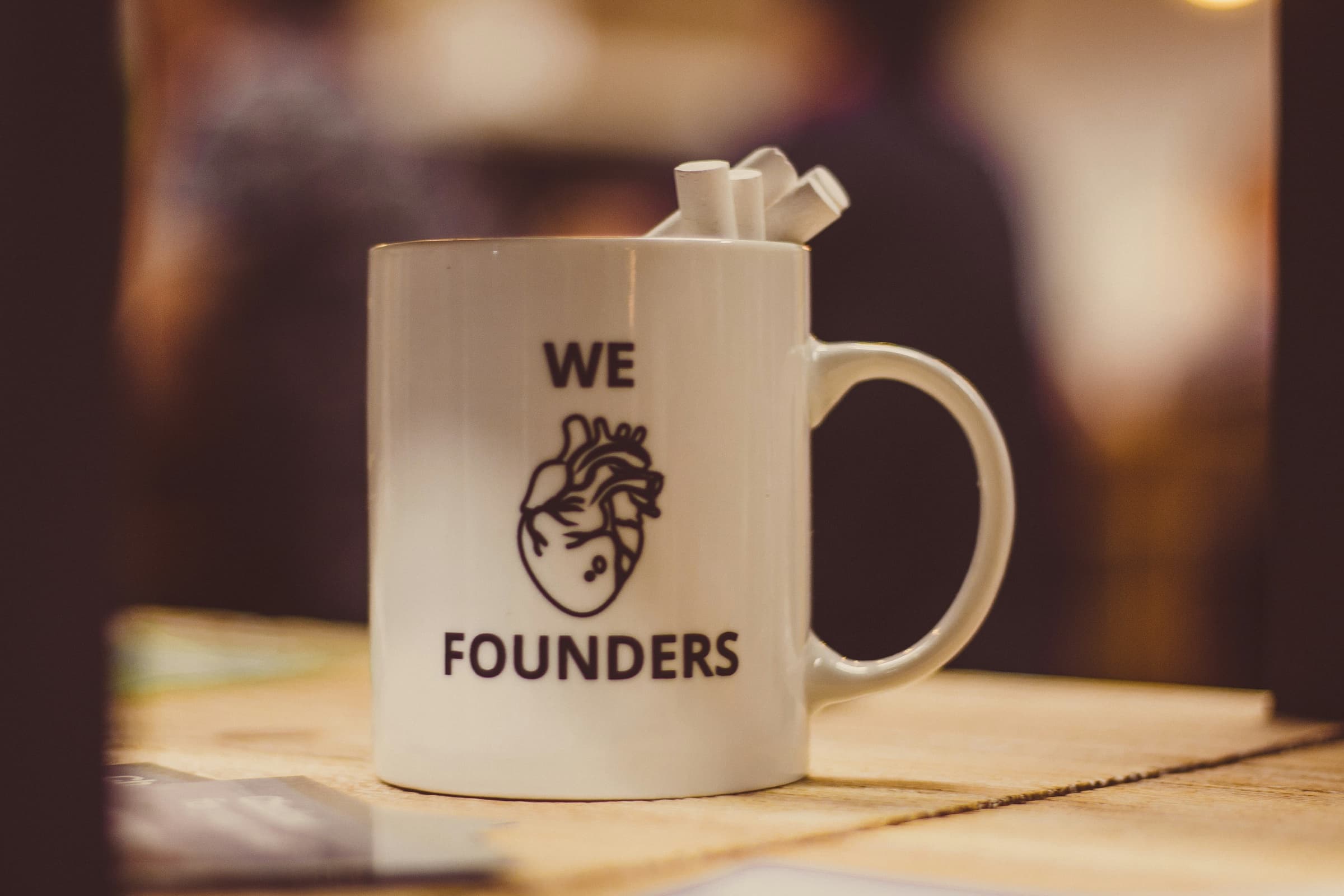 A white mug printed with "We love founders" and an anatomical heart, on a wooden table