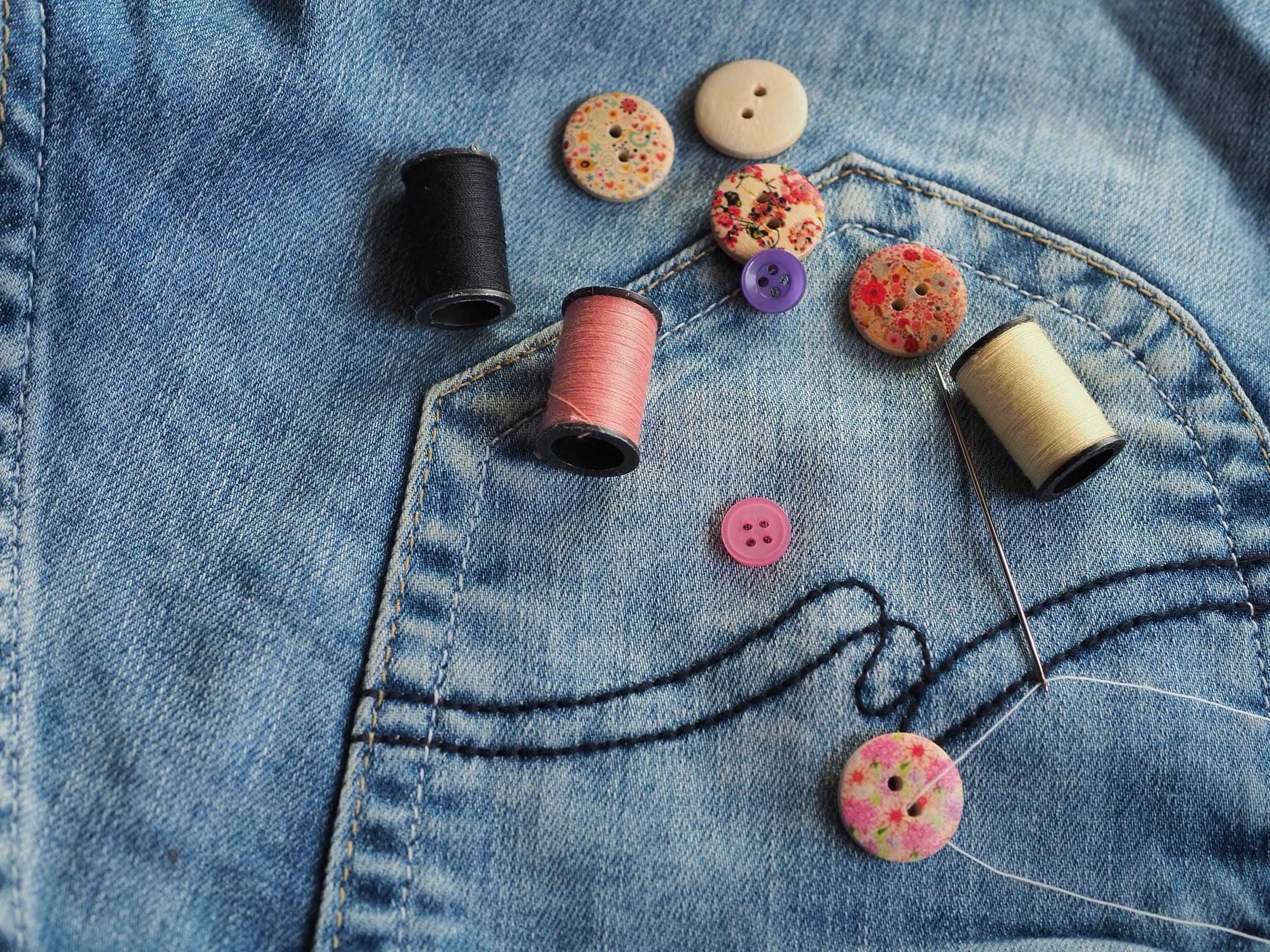Buttons, thread and a needle on the pocket of a pair of jeans