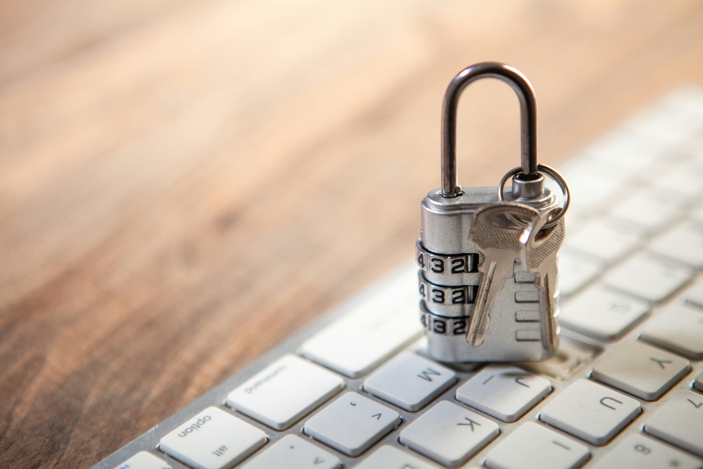 A combination padlock with keys resting on a laptop keyboard