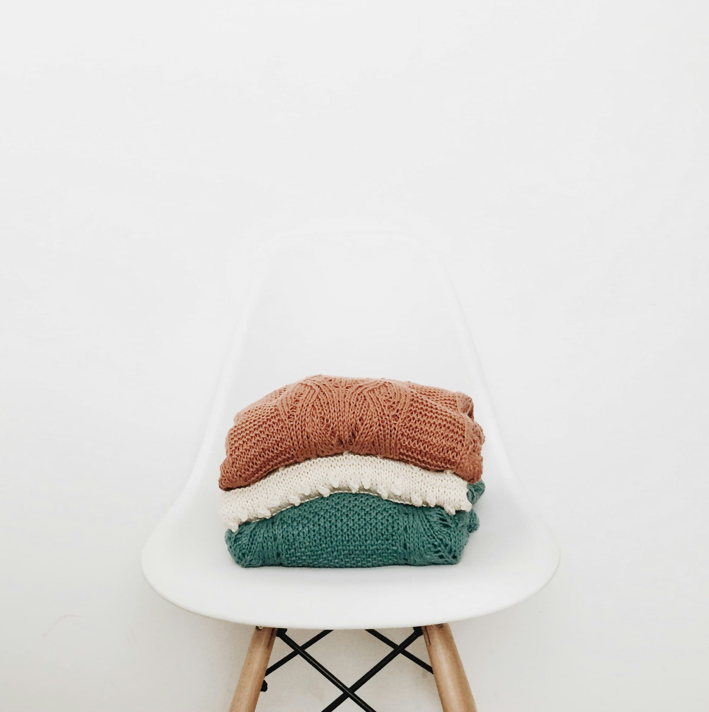 Three folded knit jumpers stacked on a white chair