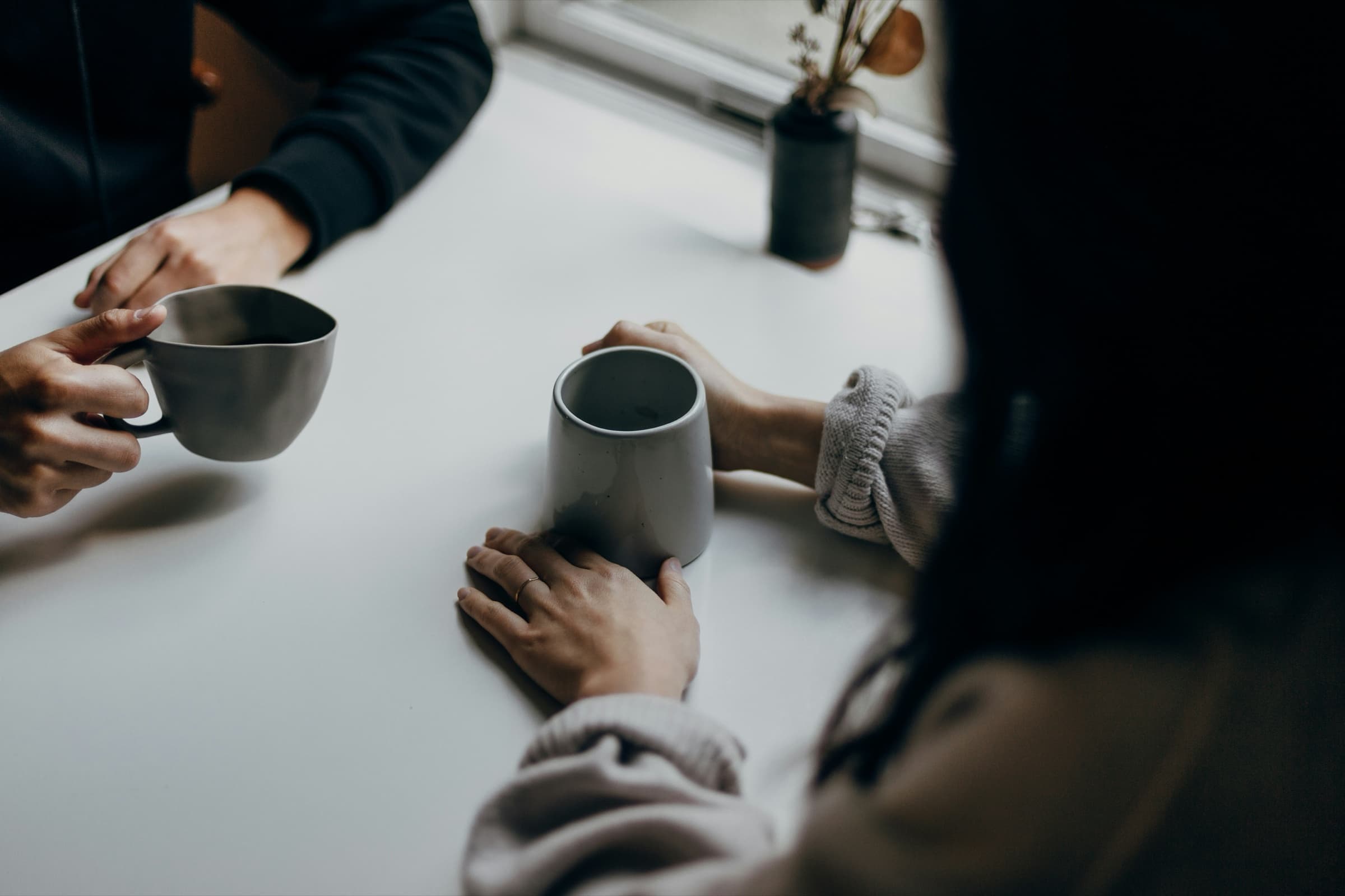 Two people talking over cups of coffee at a white table