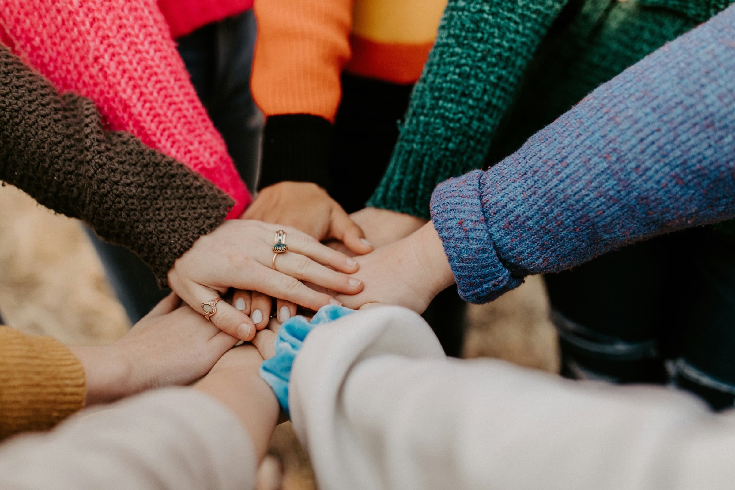 A group of people in colourful jumpers stacking their hands together